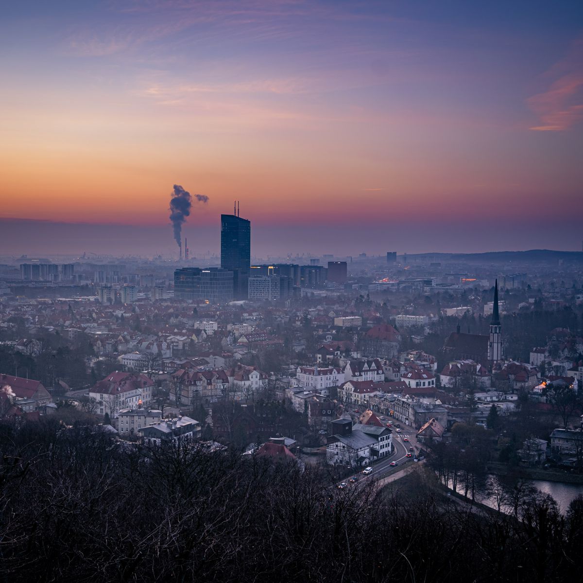 Panorama miasta o zmierzchu z dymem z komina i wieżowcem